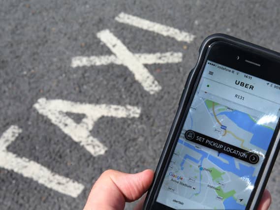 A person holds a mobile phone displaying a taxi app at a taxi rank