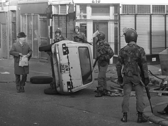 Troops on patrol in the Falls Road area of Belfast encounter a civilian by an overturned car that formed a barricade during rioting in 1981